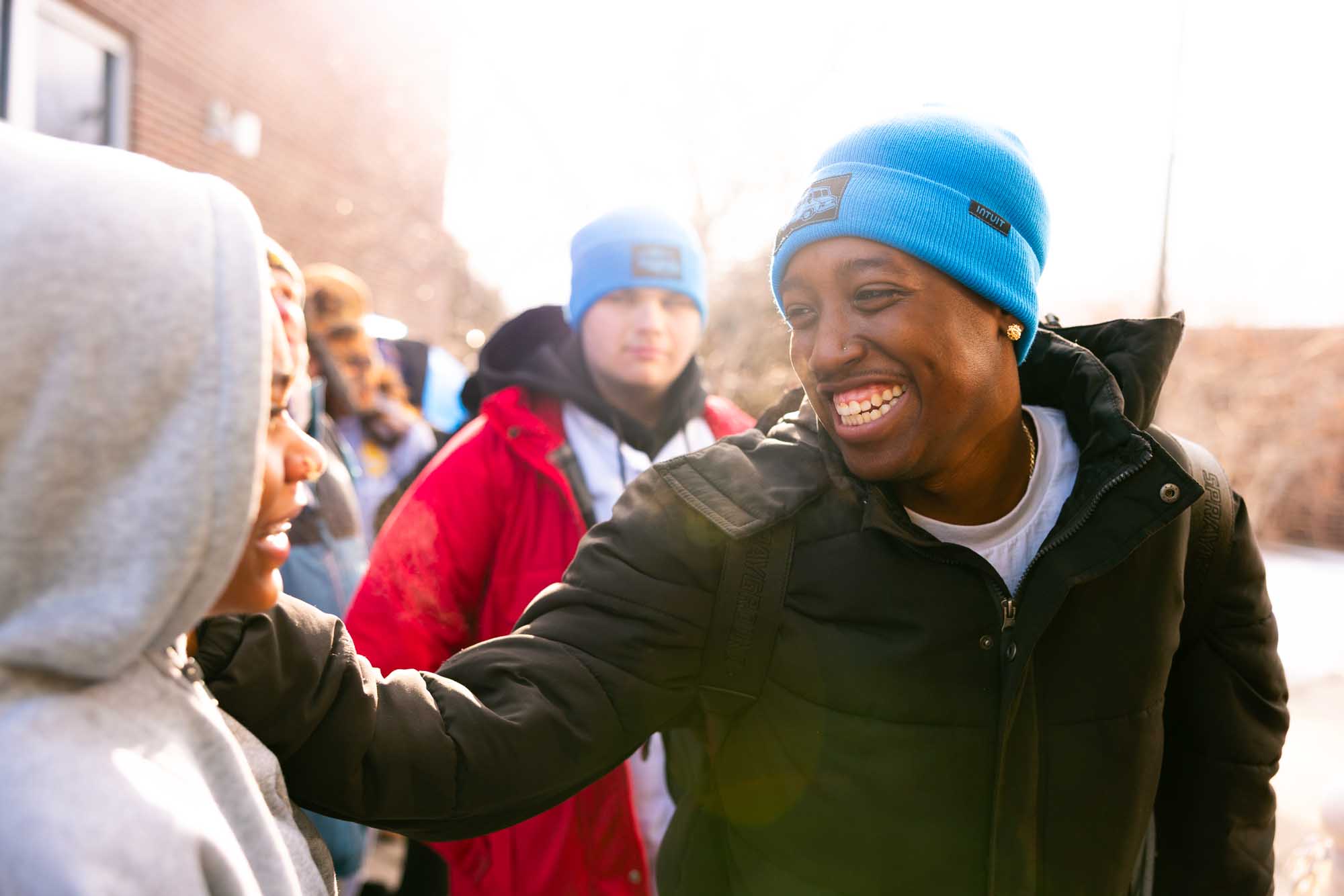 Candid moment at an outdoor branded corporate event in Denver — attendees in Intuit beanies greeting each other.