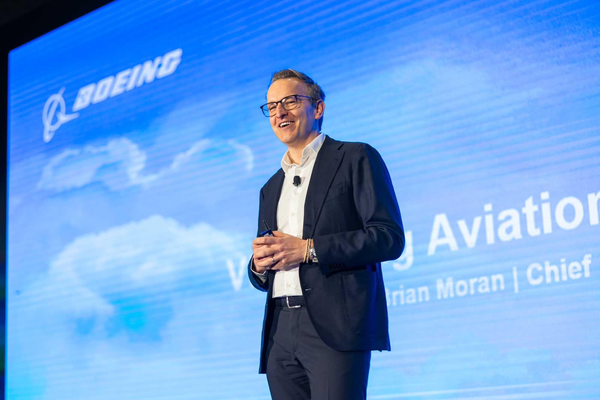 Boeing keynote speaker smiling on stage at a corporate aviation conference in Denver.
