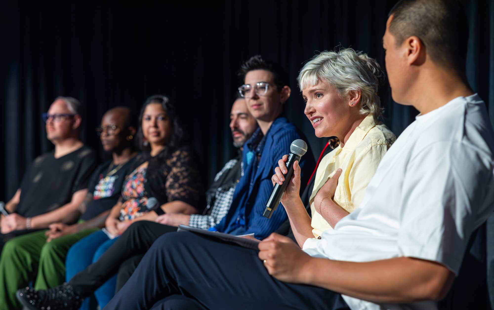 Panel discussion on stage at a Denver corporate conference, one panelist speaking into a handheld microphone.