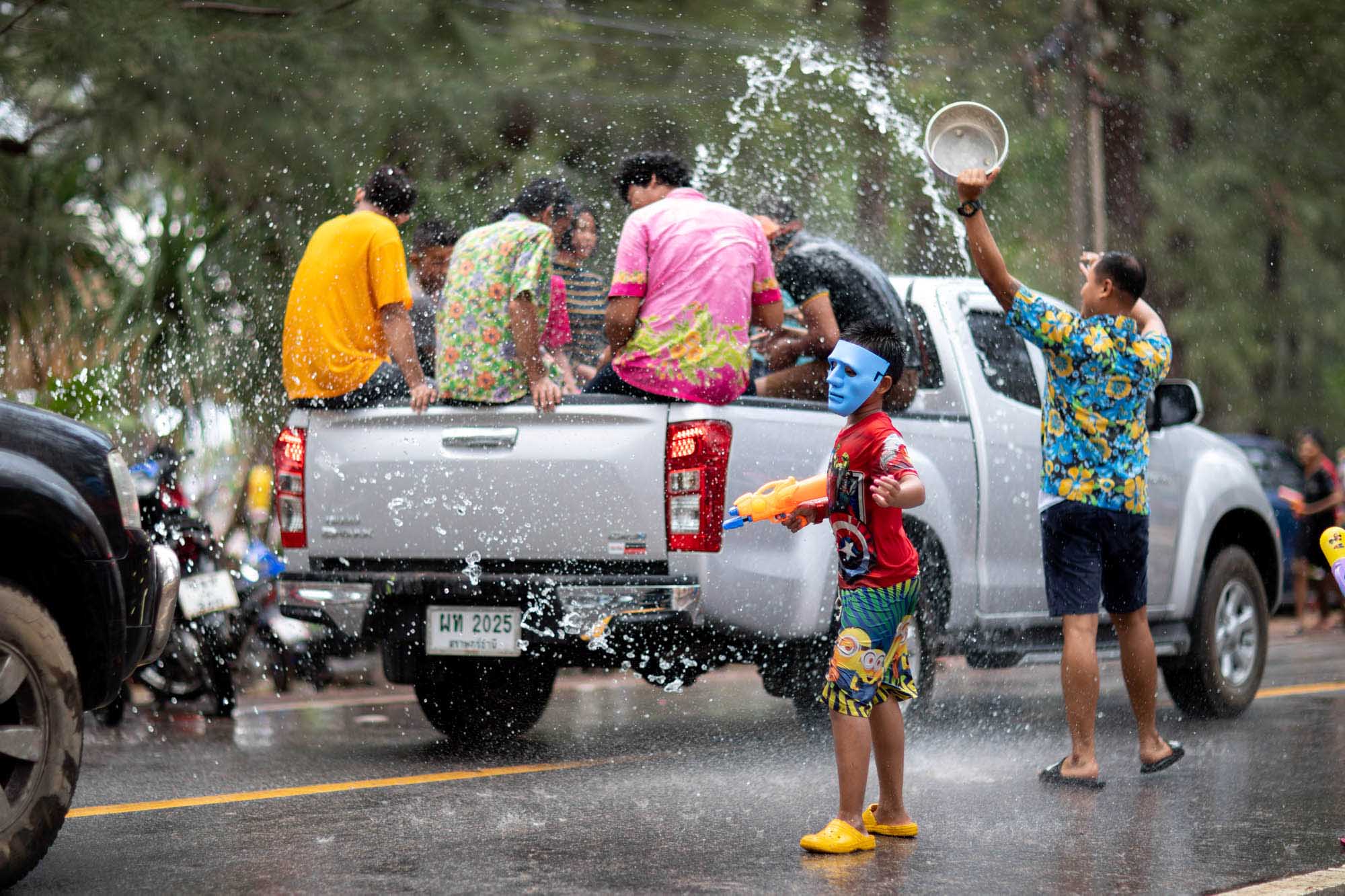 Boy wearing a mask and taunting a truck during water fight at Songkran water festival in Phuket, Thailand