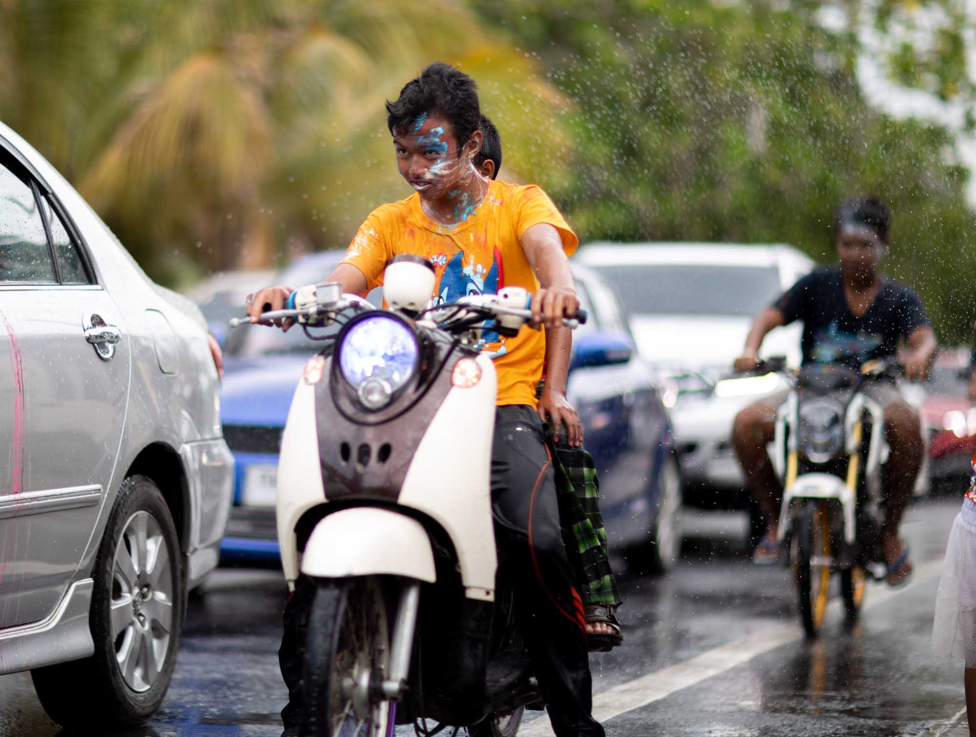 Boy dodges water on motorbike at Songkran water festival in Phuket, Thailand