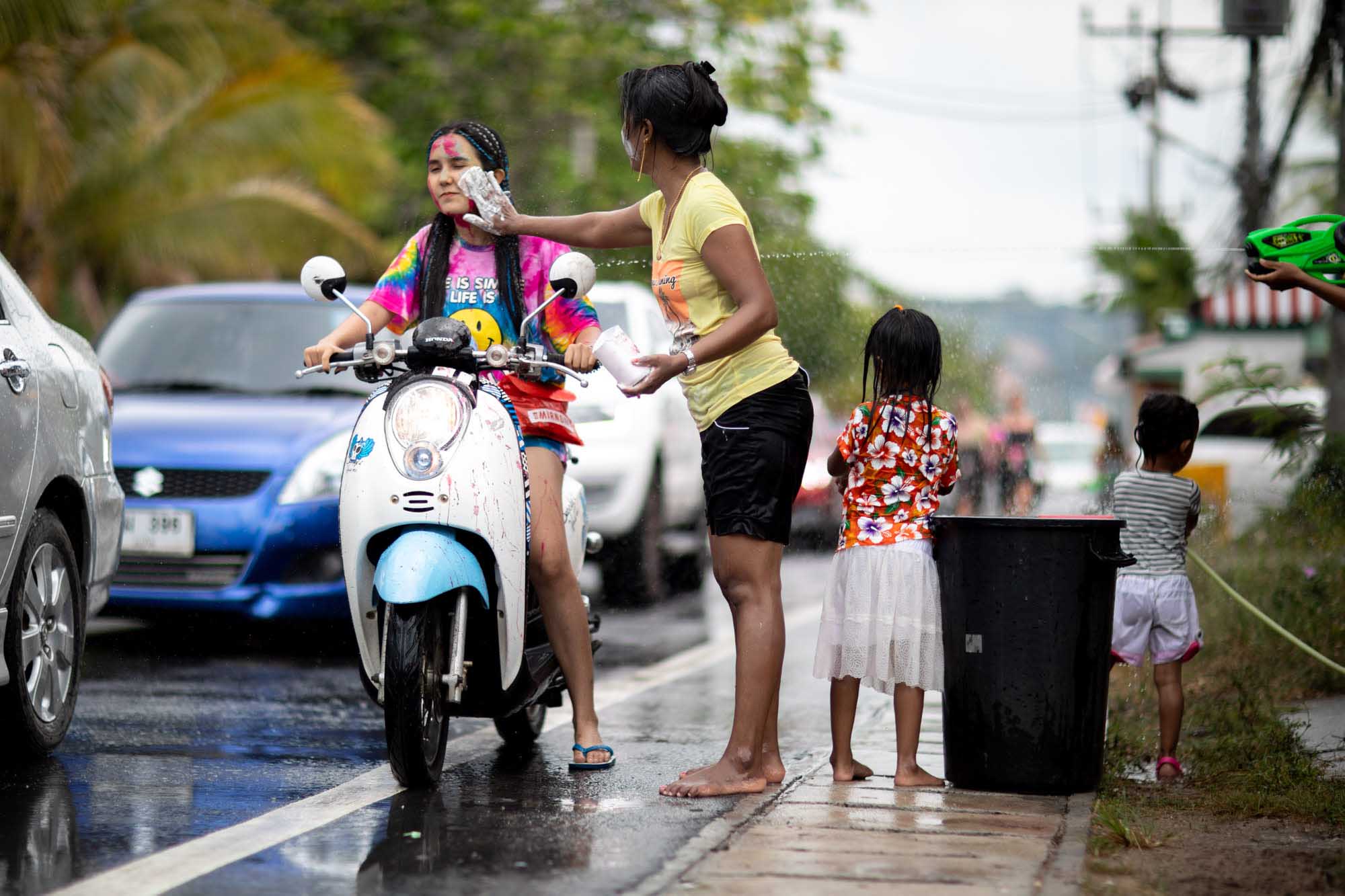 Young woman gets face painted while riding motorbike at Songkran water festival in Phuket, Thailand