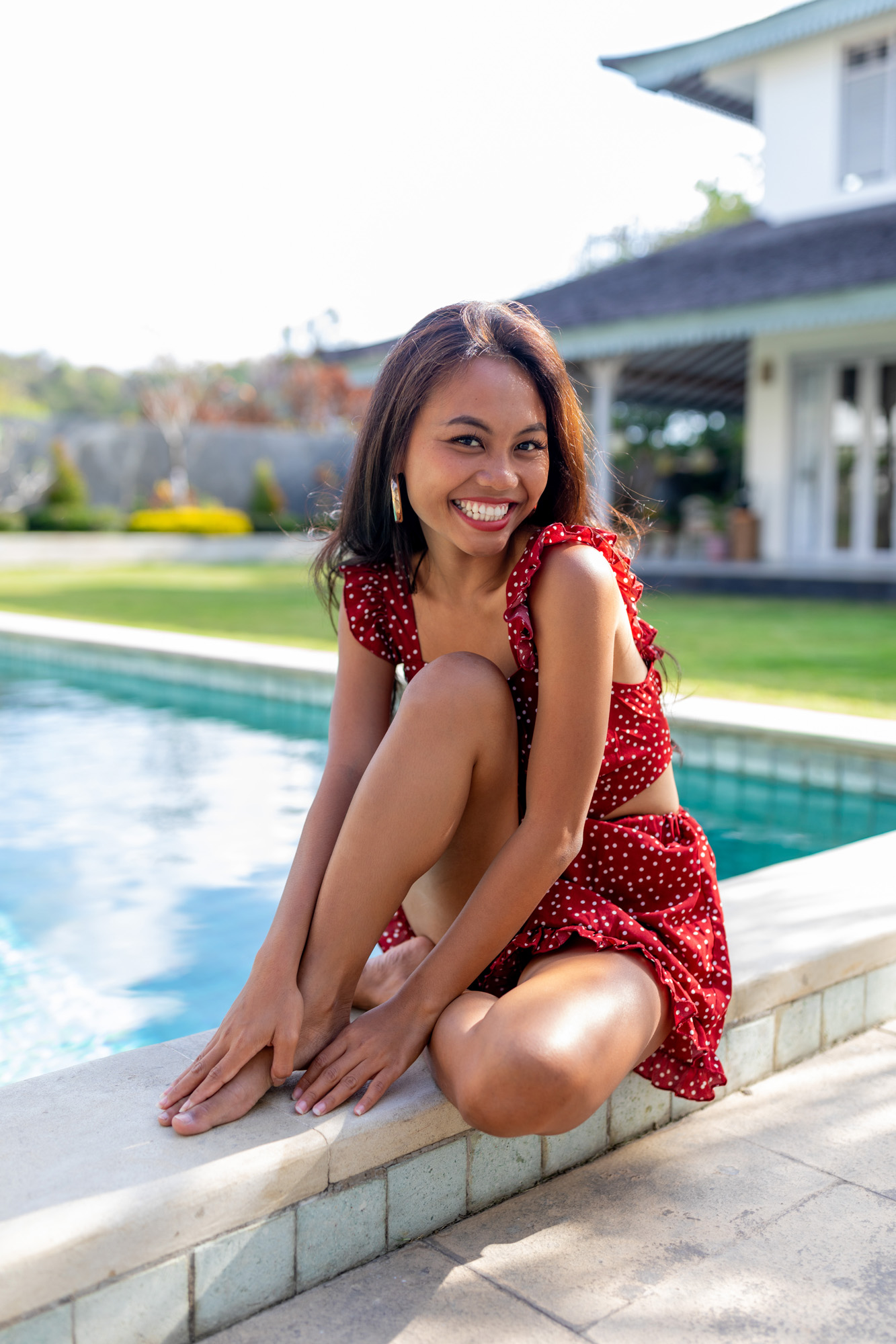 Woman wearing red sits by pool and smiles playfully | Lifestyle Photography | Swimwear Photography | Asian Bali Model | High Key Photography | Fashion Photography