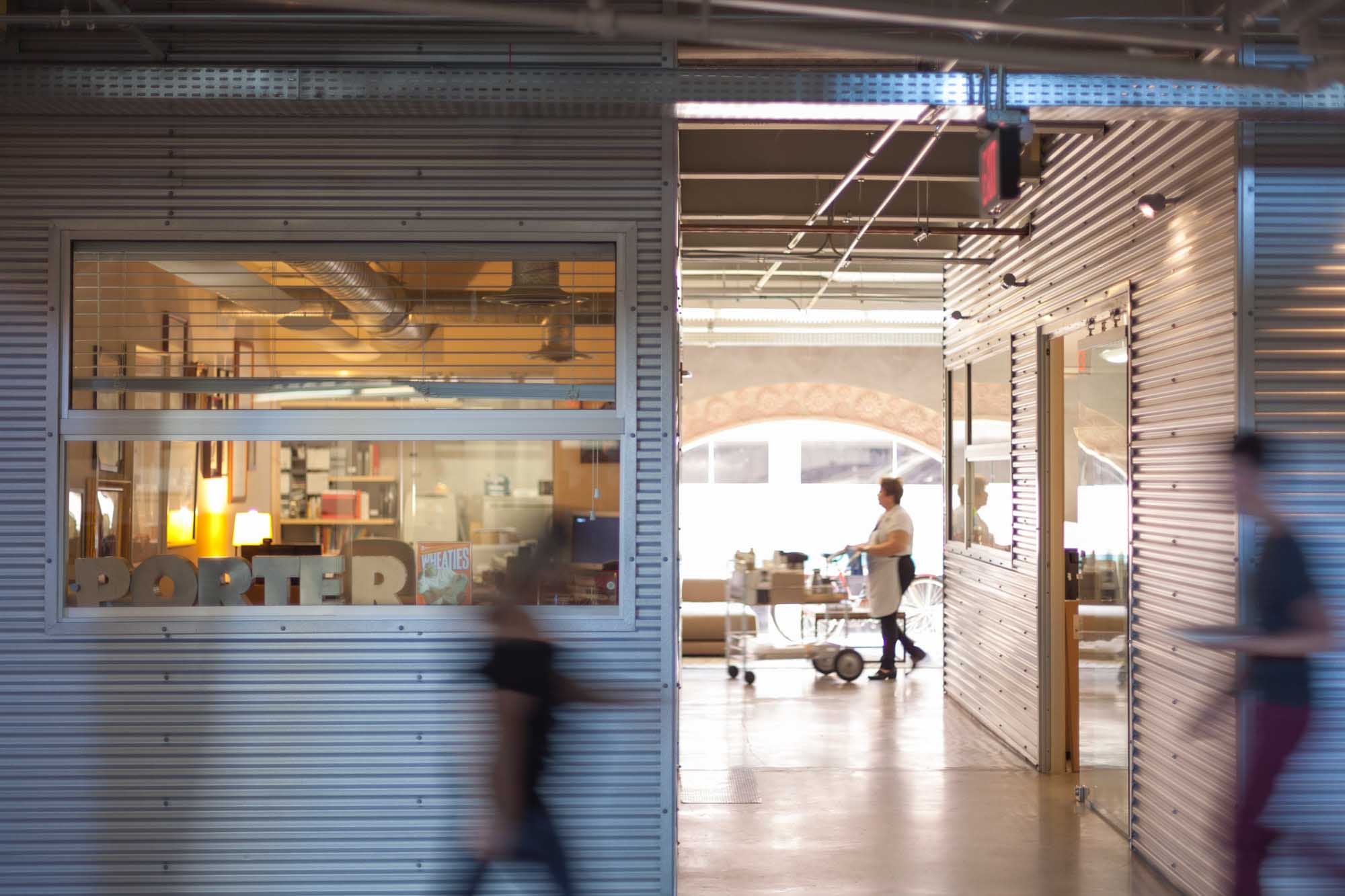 Corrugated-metal hallway inside the CP+B Miami office, staff blurred mid-stride walking past.