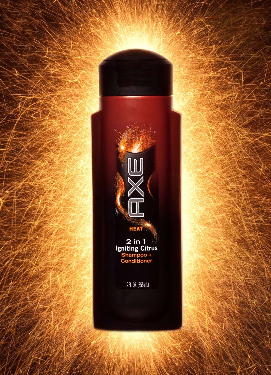 Studio product photograph of an Axe Heat 2-in-1 Igniting Citrus shampoo bottle framed by a burst of orange sparks on a black background.