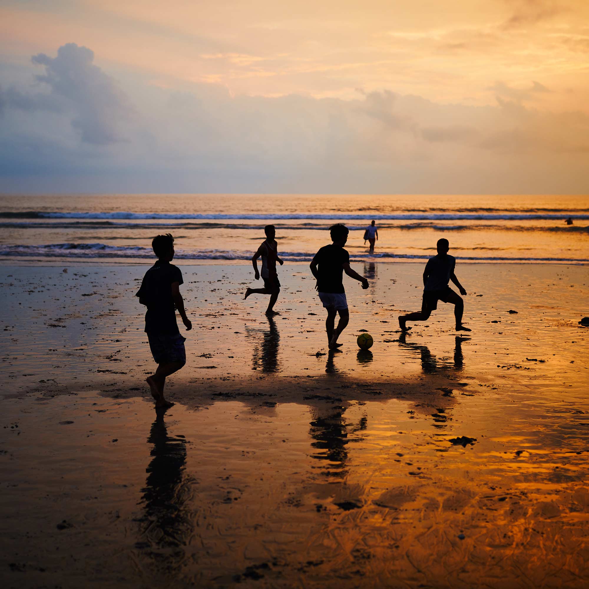 Silhouettes of kids playing pick-up soccer on a wet Kuta Beach at sunset, Bali, Indonesia.