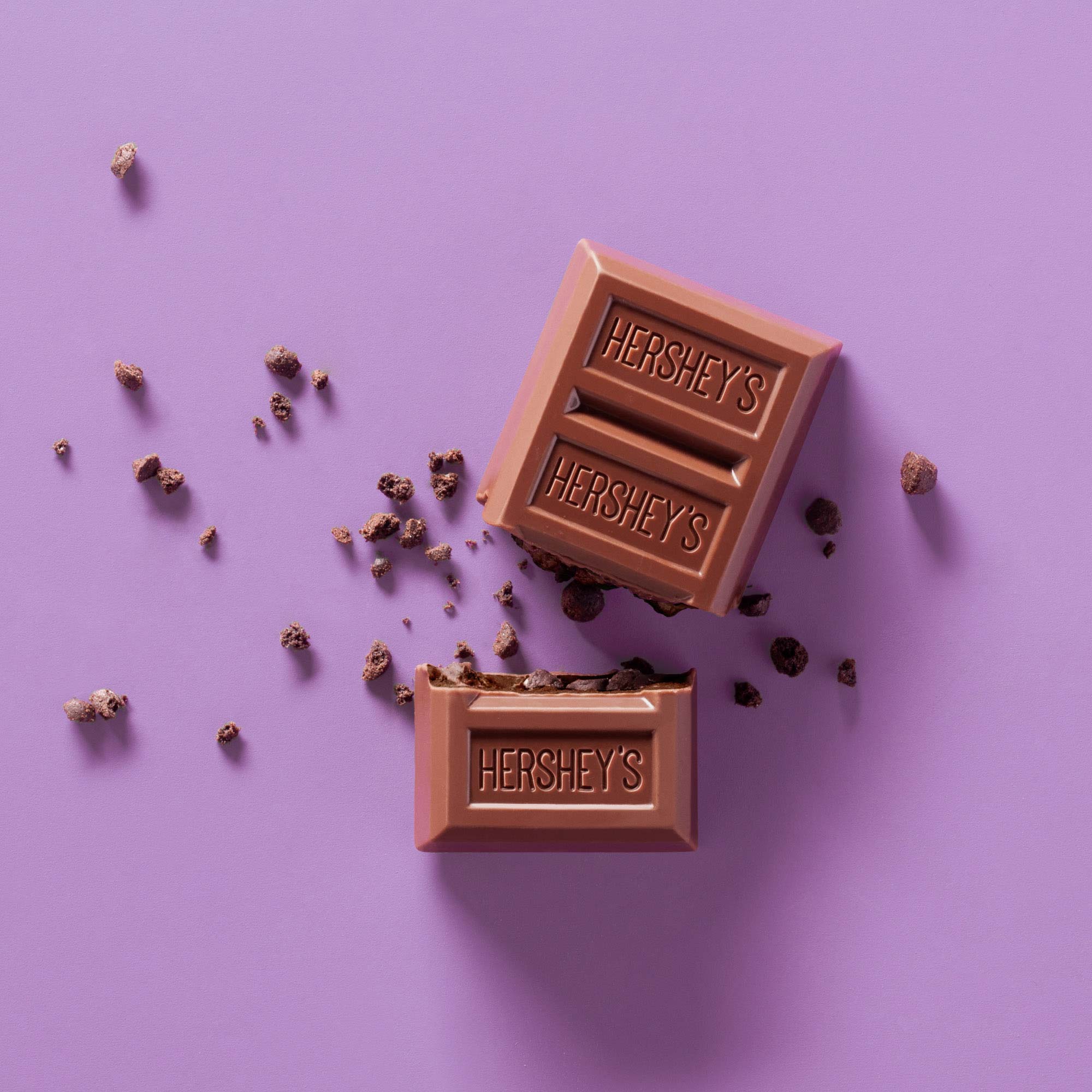 Studio product photography of a Hershey’s chocolate bar broken into pieces on a purple background