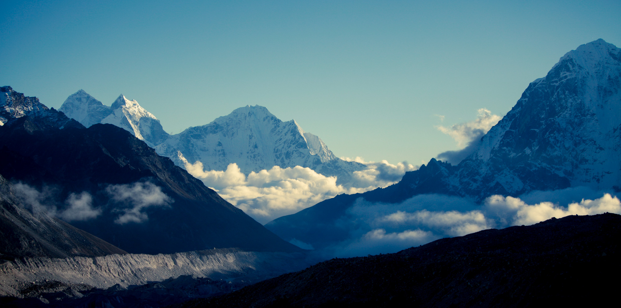 Late-afternoon light over layered Himalayan ridgelines with snow-capped peaks rising behind drifting clouds in the Khumbu Valley, Nepal.