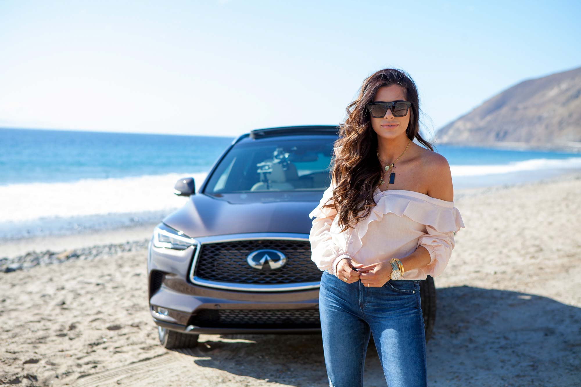 Lifestyle automotive photography for Infiniti featuring a woman standing in front of an SUV at the beach.