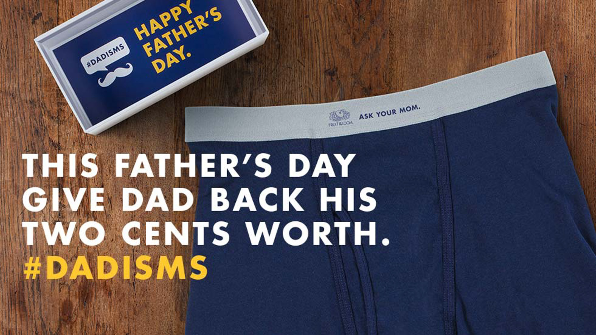 Father's Day social ad for Fruit of the Loom — a #DADISMS gift box beside a navy pair of men's underwear with the line 'Give Dad back his two cents worth' on a dark wood surface.
