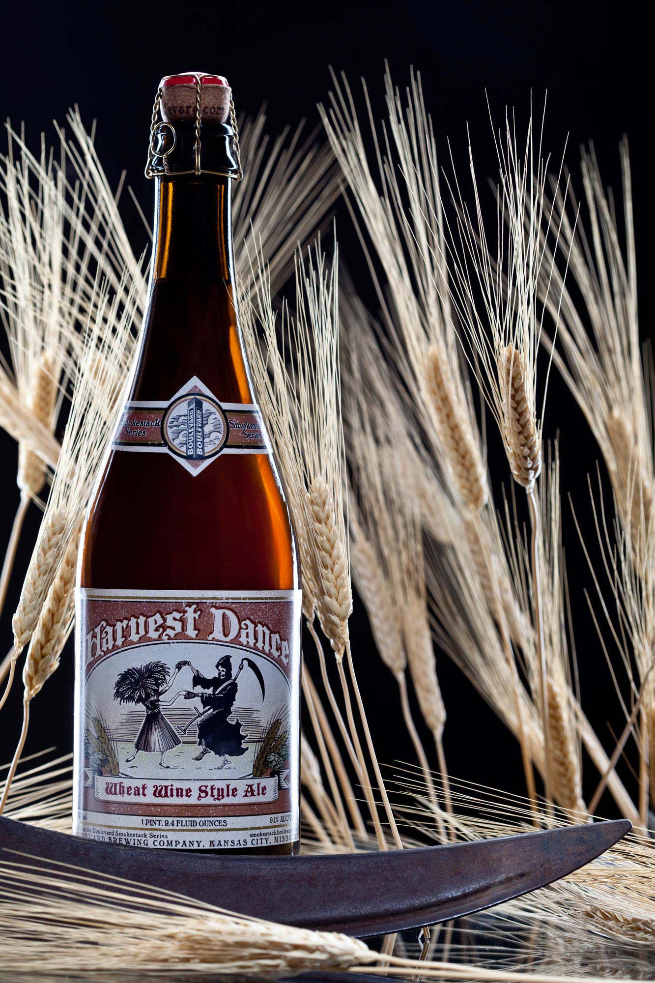 Product photography of a Harvest Dance wheat wine style ale bottle surrounded by wheat