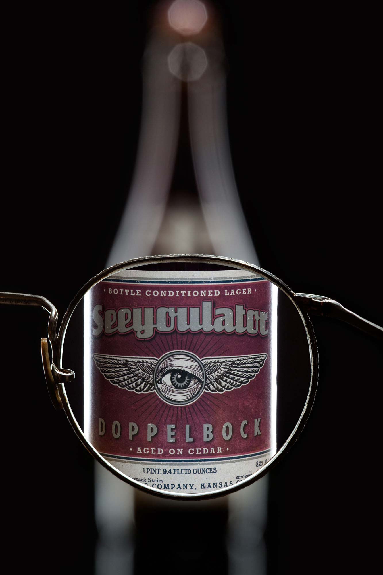 A bottle of See You Later Doppelbock photographed through a pair of eyeglasses that bring the label into sharp focus against a dark studio background.