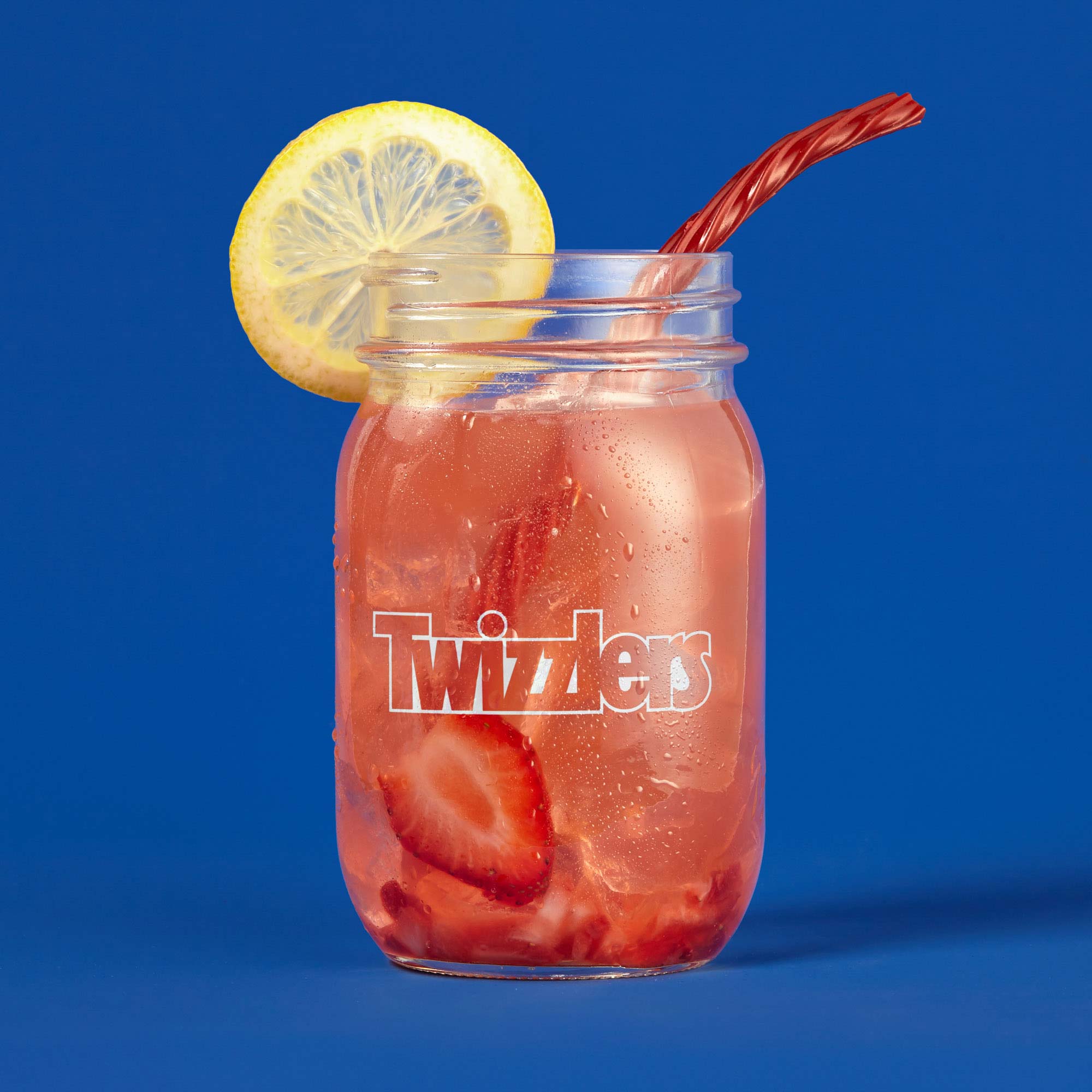 Studio product photography of a Twizzlers drink featuring strawberries and lemon in a mason jar on a blue background