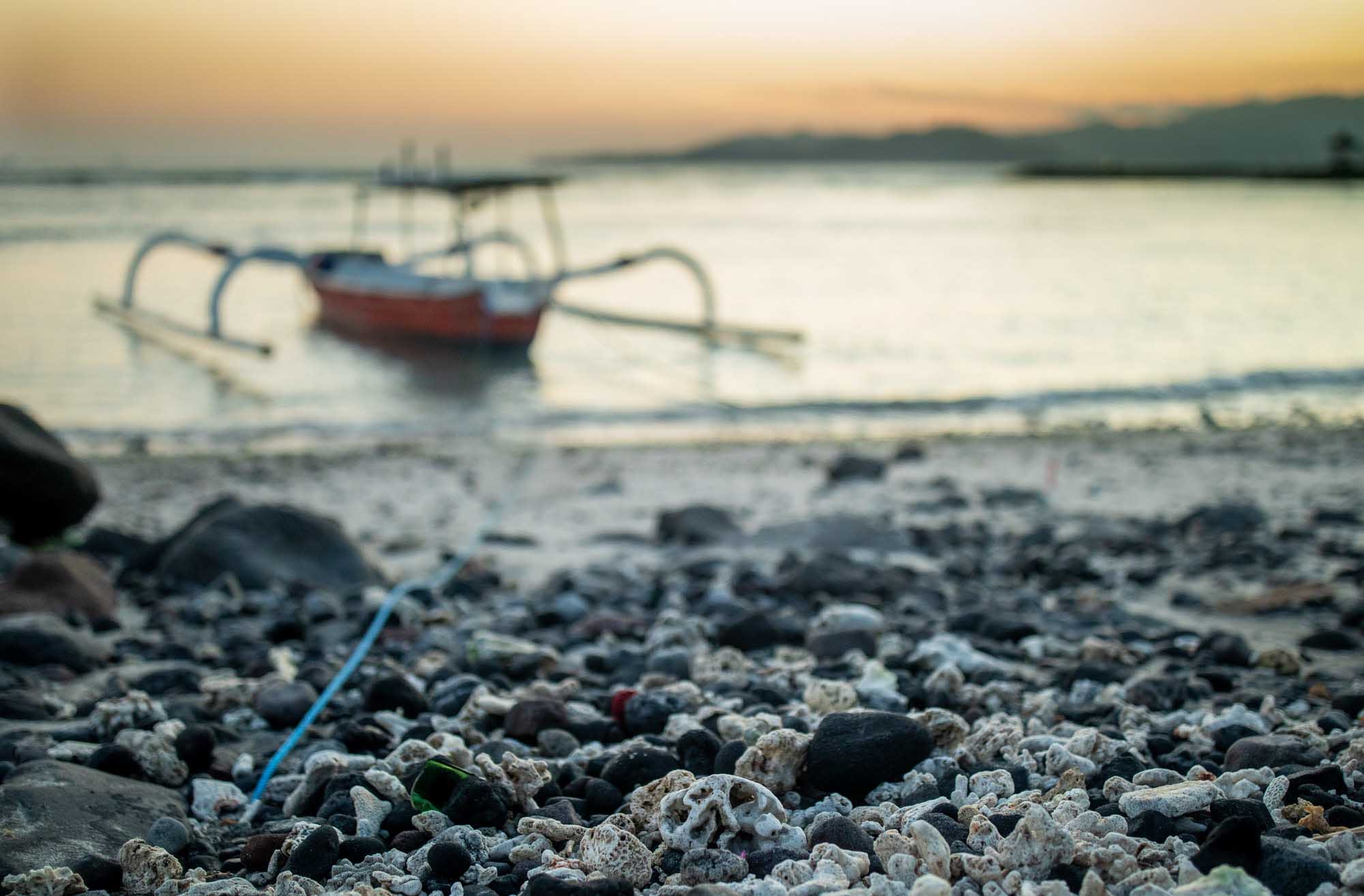 A traditional Balinese outrigger jukung moored on a pebble and coral beach at dusk in Candidasa, Bali.