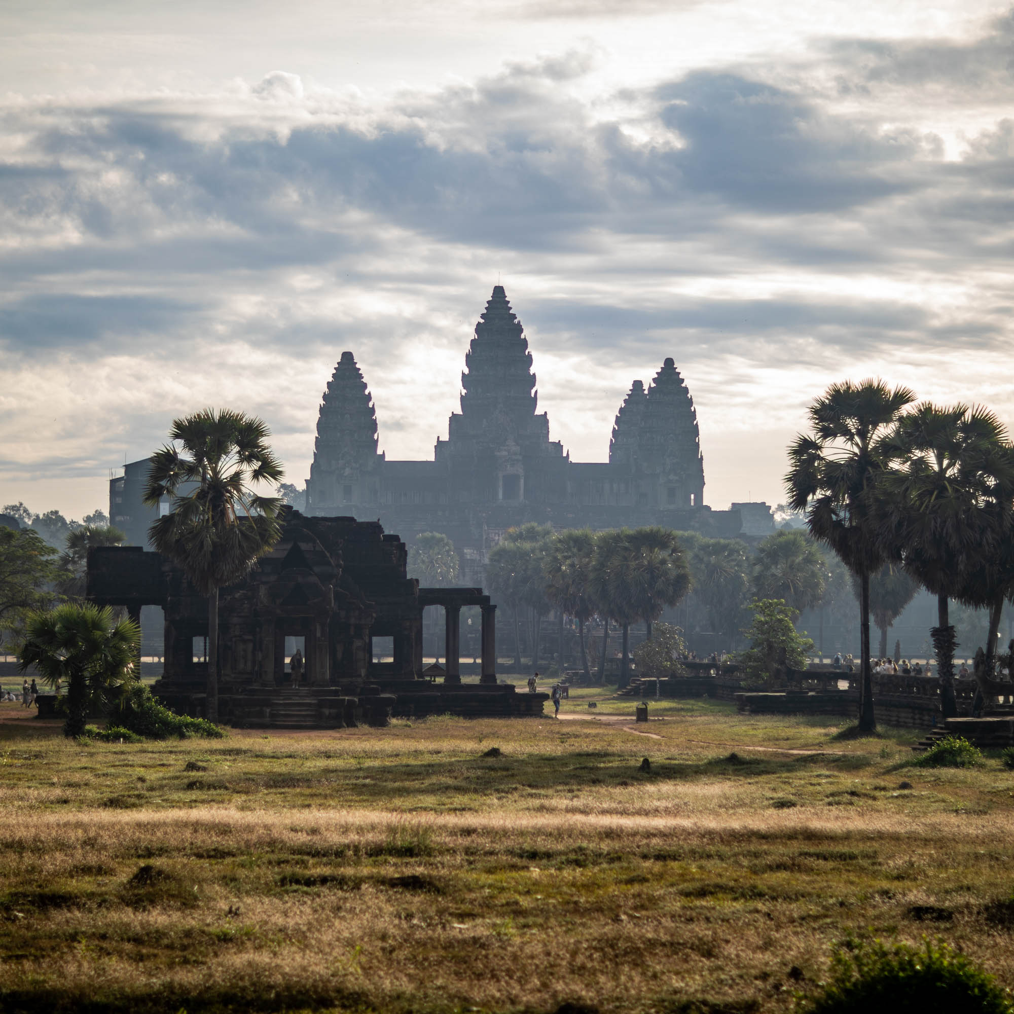 Angkor Wat silhouetted against soft morning cloud cover, viewed across the grounds at sunrise — Siem Reap, Cambodia.