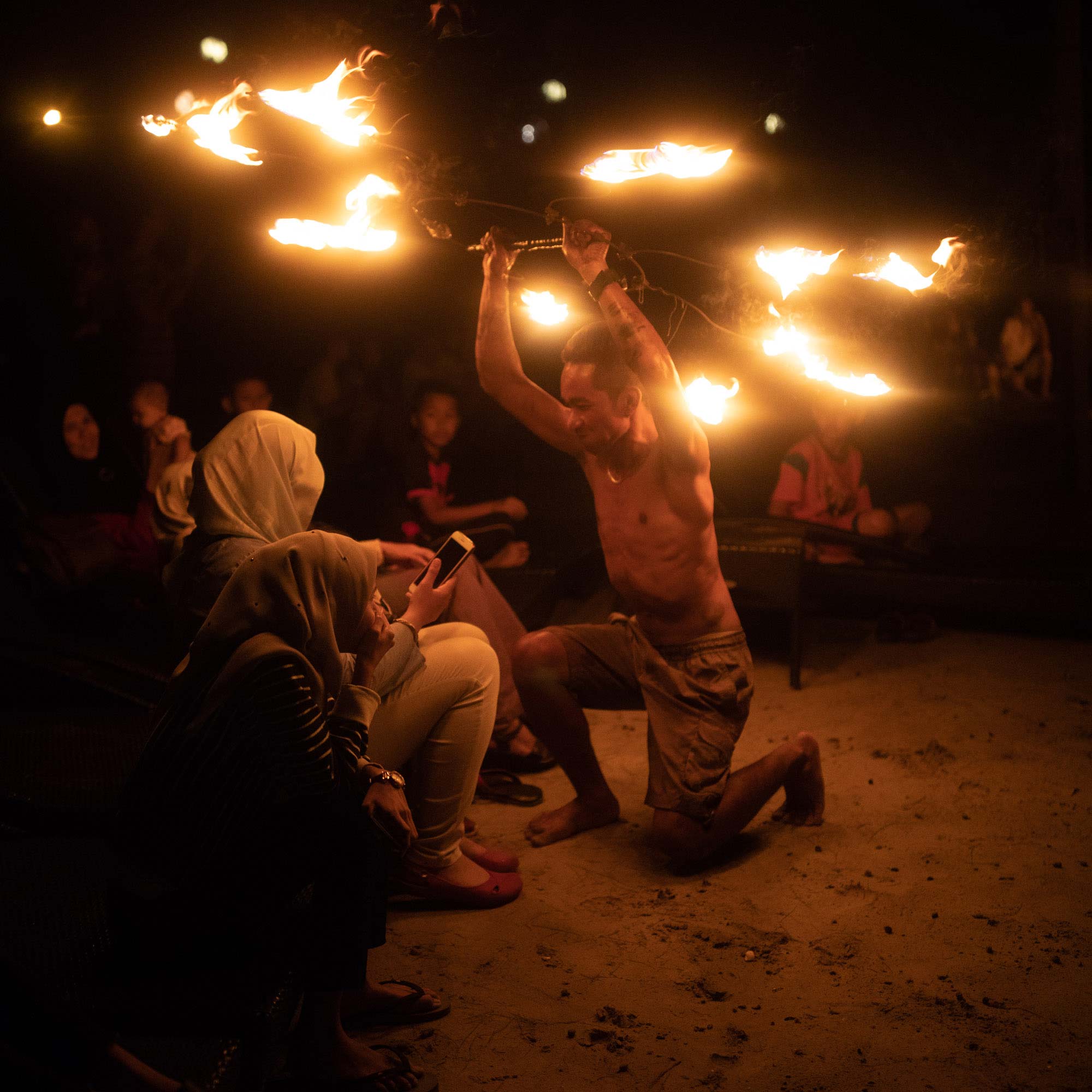 Cultural performance featuring a fire dancer entertaining an audience at night.