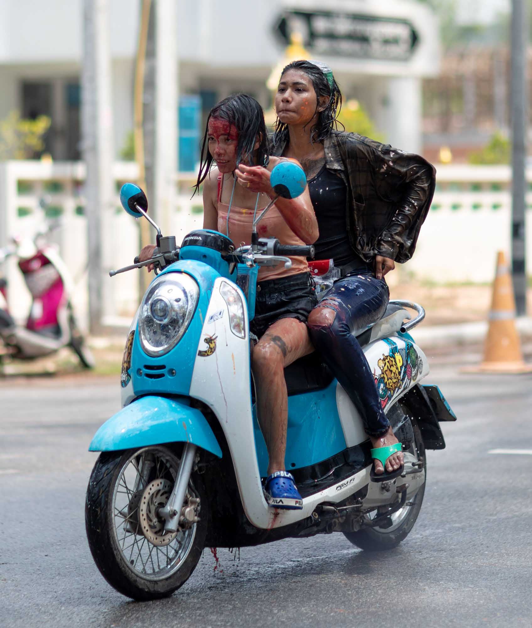 A young woman rides a red scooter down a Phuket street, her face painted with pink powder, during the Songkran water festival.