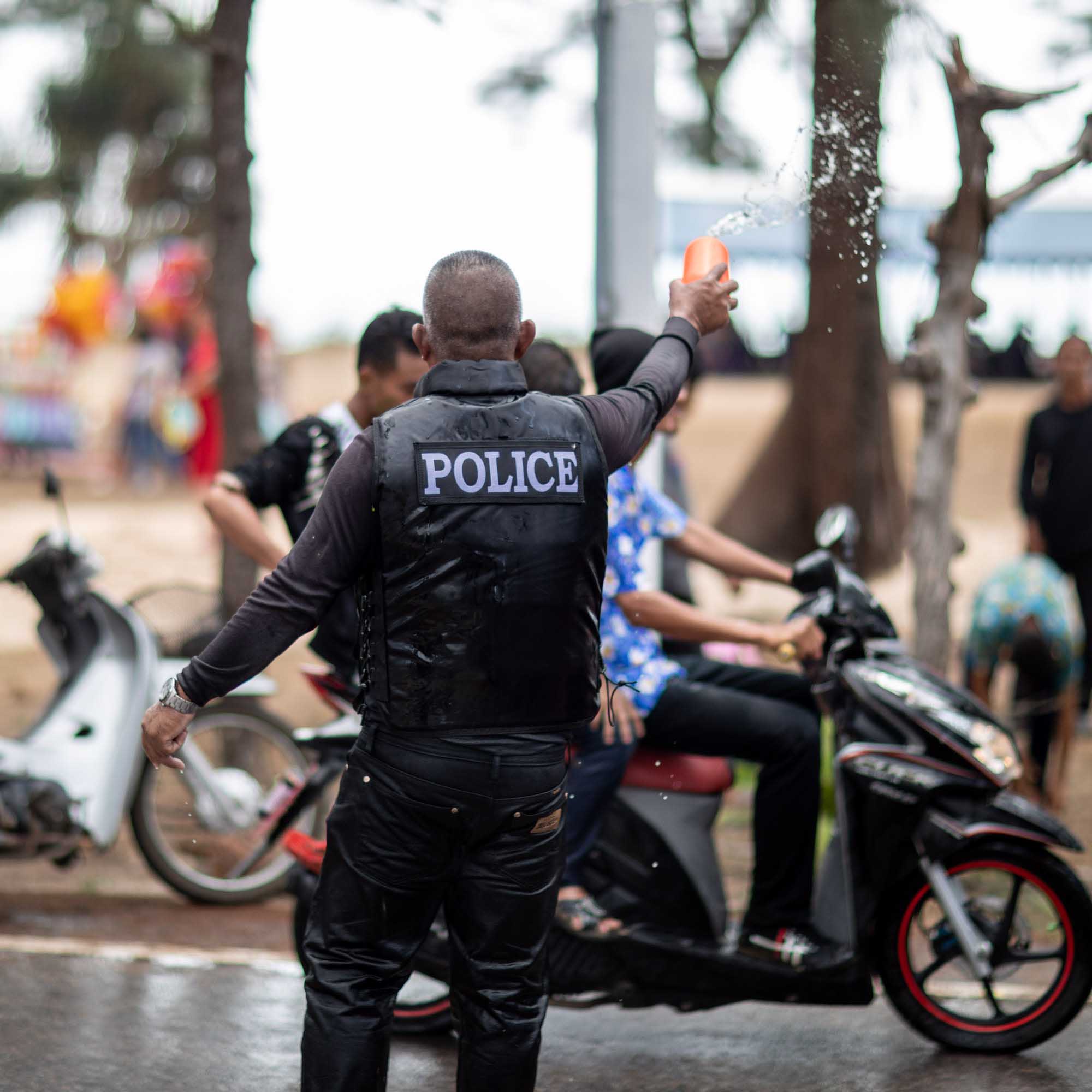A Thai police officer in a tactical vest tosses a splash of water from a plastic bucket toward a passing motorbike during the Songkran water festival in Phuket.