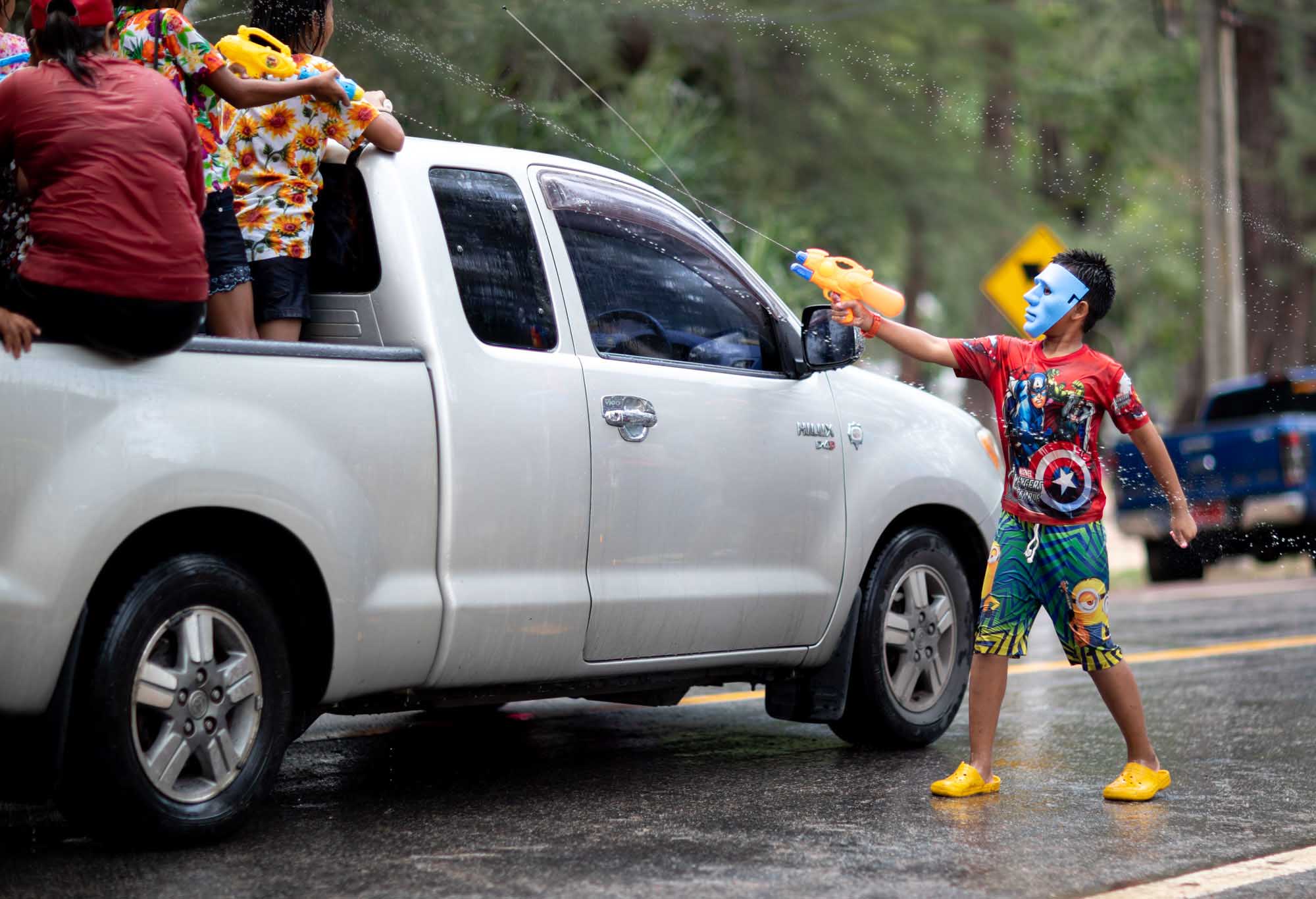 A boy in a blue skeleton face-mask and Captain America shirt fires a yellow water gun at a passing pickup truck during the Songkran water festival in Phuket, Thailand.