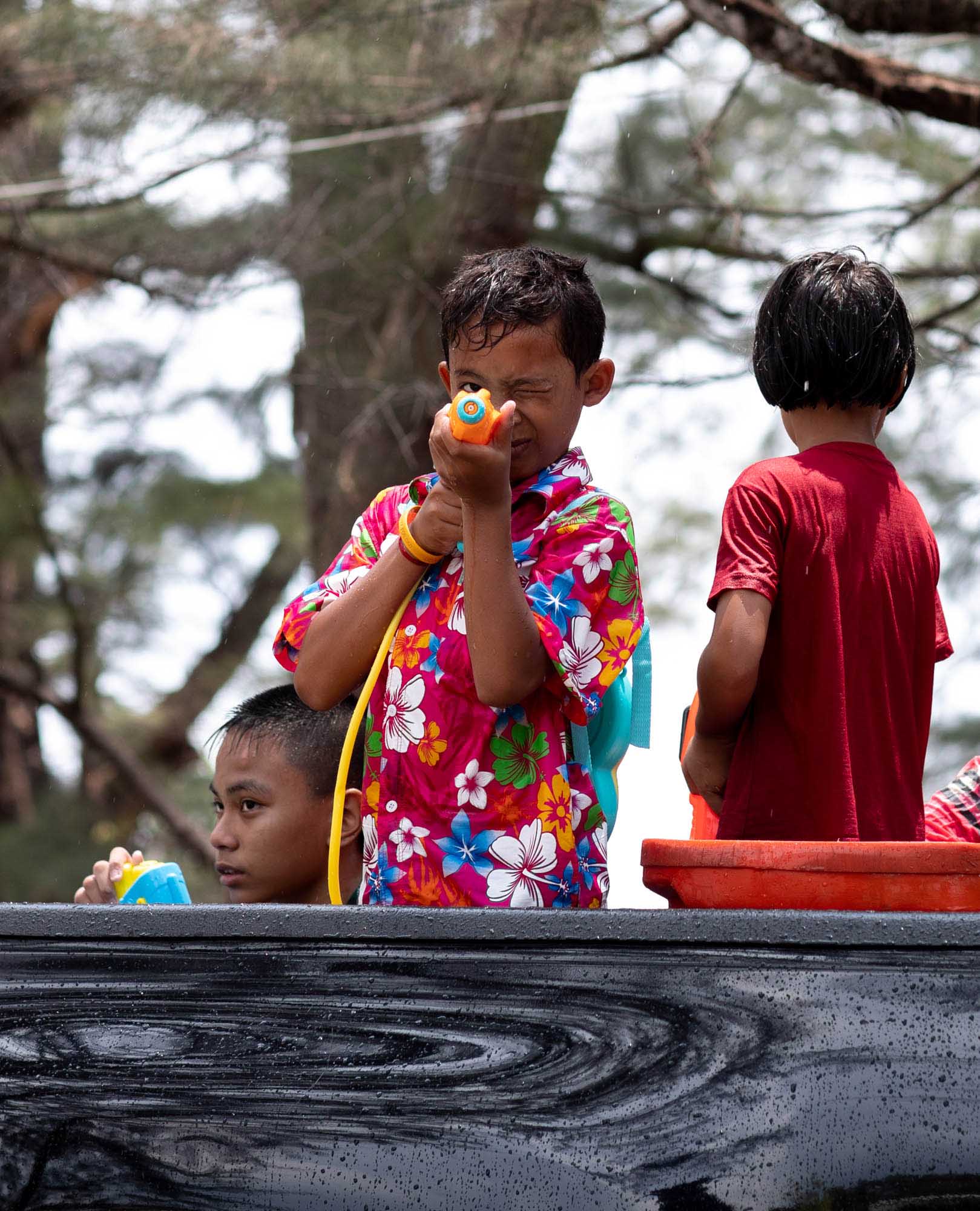 A boy in a bright Hawaiian shirt aims a small orange water gun from the back of a pickup truck during the Songkran water festival in Phuket, Thailand.