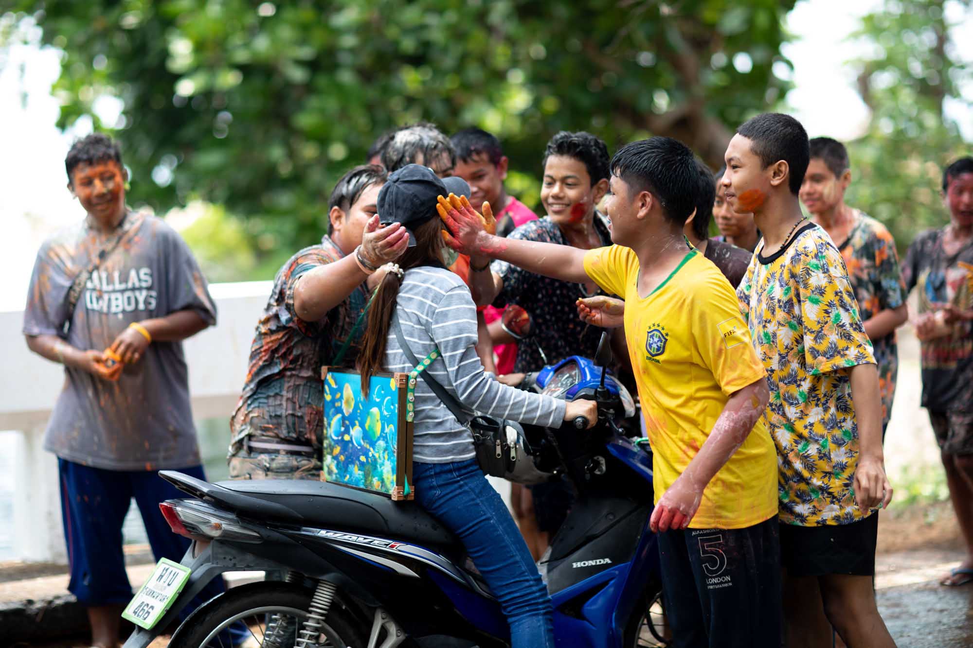 A young woman on a scooter gets red powder smeared across her cheek by a friend during the Songkran water festival in Phuket, Thailand.