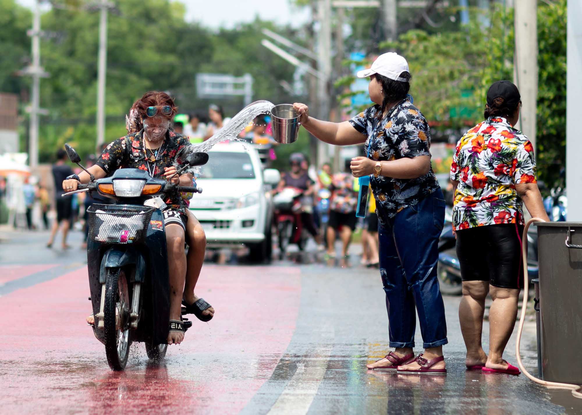 A Thai woman flings water from a metal bowl at a passing scooter during the Songkran water festival in Phuket, Thailand.