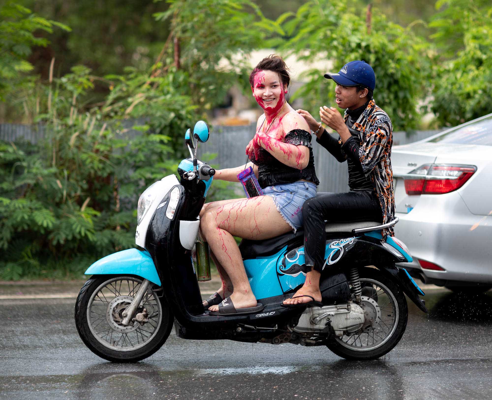 Woman covered in red paint drives motorbike at Songkran water festival in Phuket, Thailand