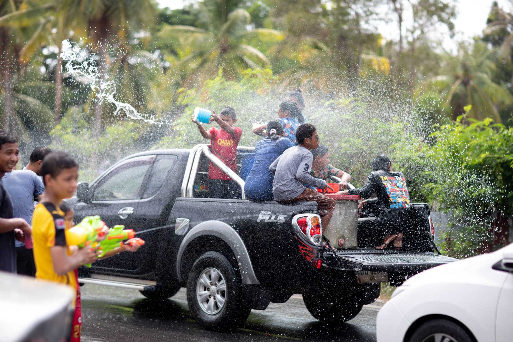 Teenage friends ride in the back of a pickup truck hurling water from buckets mid-convoy during the Songkran water festival in Phuket, Thailand.